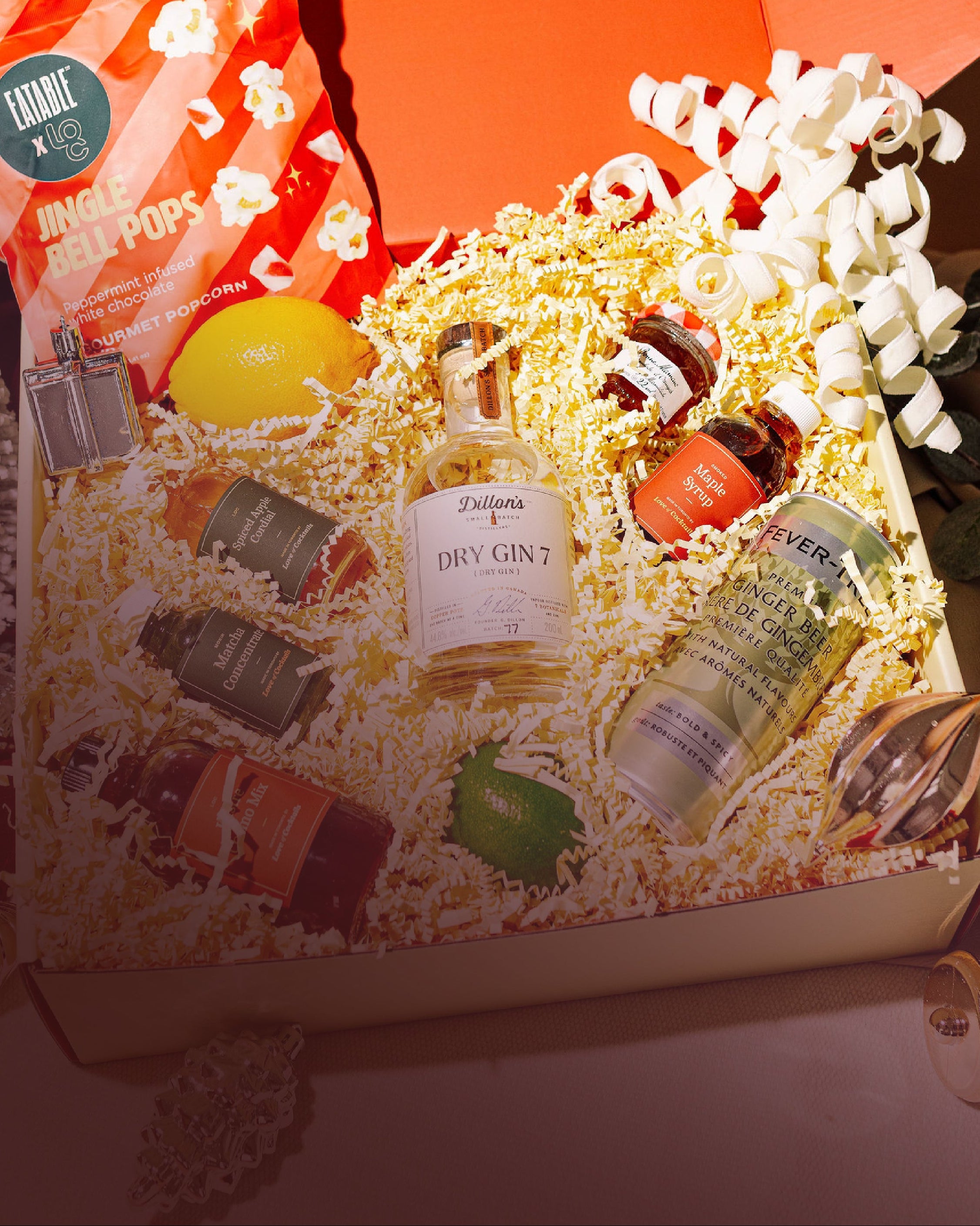 Open gift box with popcorn, snacks, and a bottle of wine on a wooden surface.