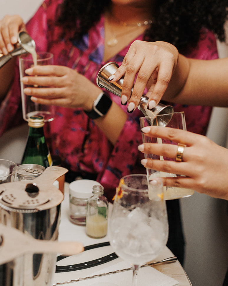 Two people preparing cocktails at a bar with ice buckets and glasses.