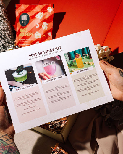 Person holding a 2025 Holiday Kit brochure with festive decorations in the background.