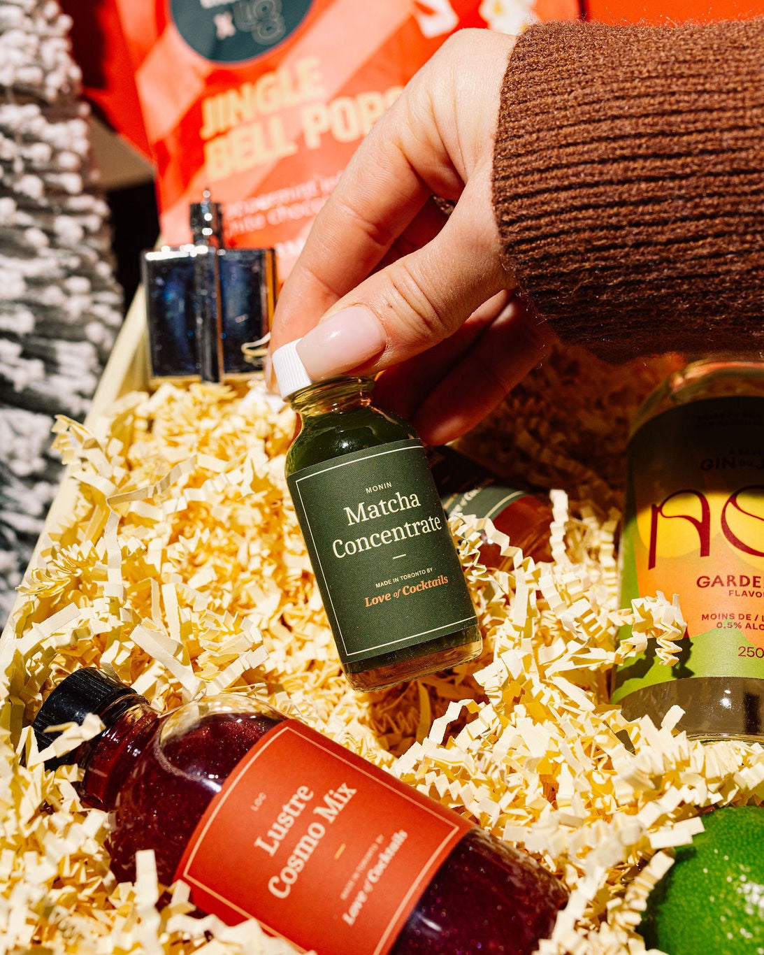 Hand holding a bottle of Matcha mixer over a gift basket with various tea products.